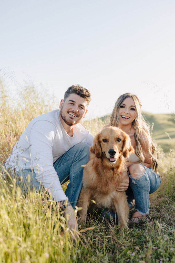 A couple leaning down in a field with their dog. 